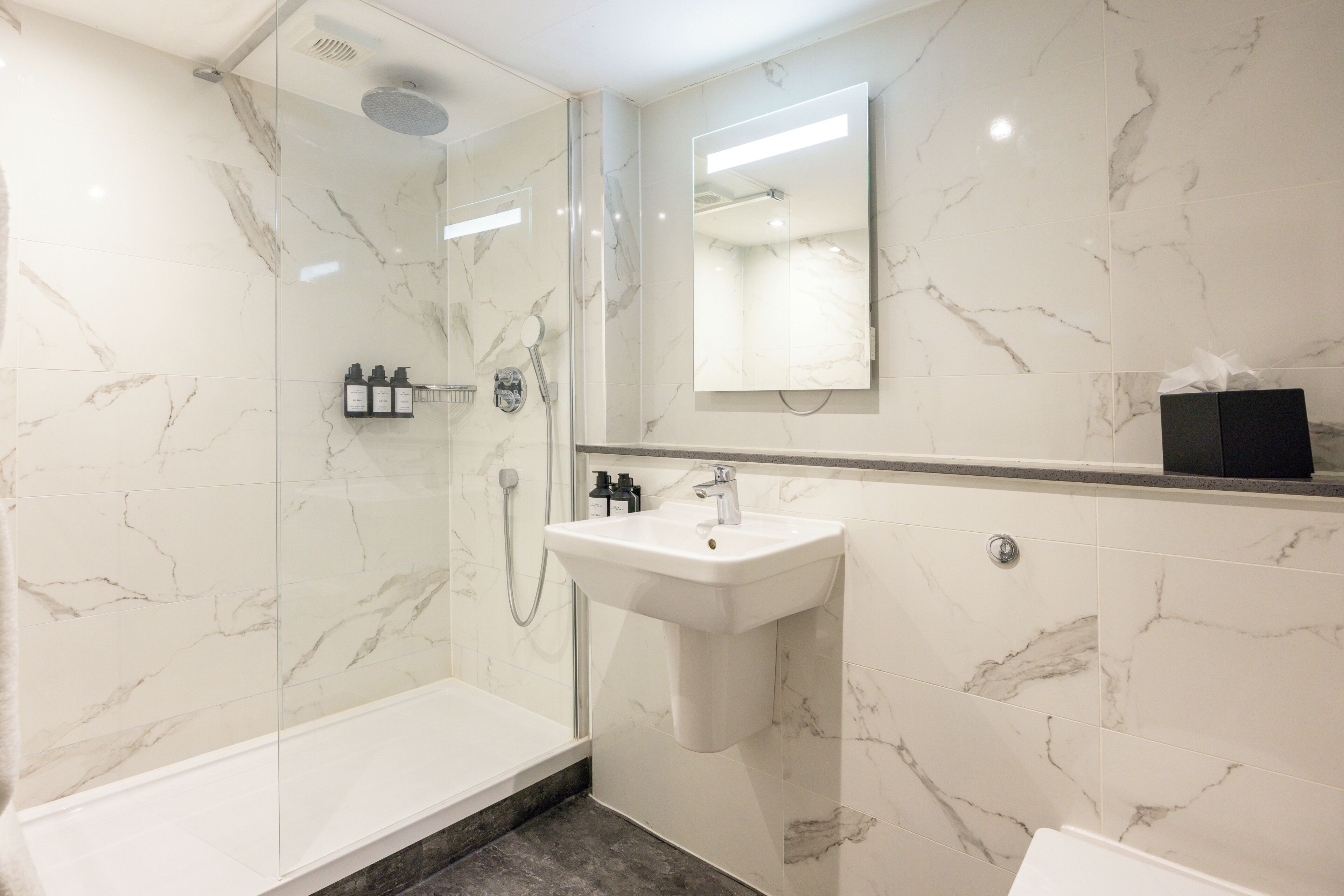 A modern bathroom with a glass-enclosed shower, a white sink, and marble walls.