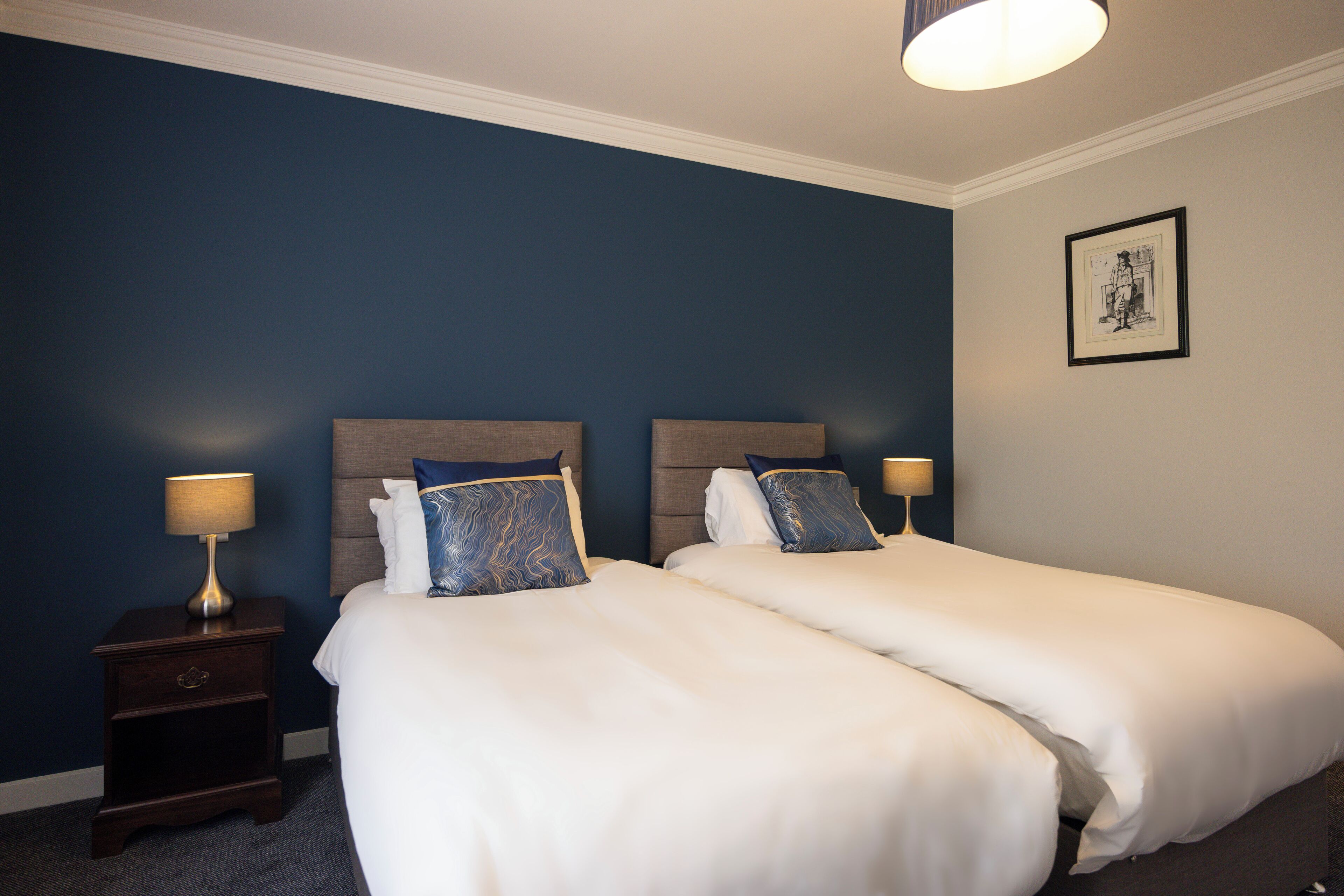 Habitación de hotel con dos camas, una mesita de noche y una lámpara de pared.