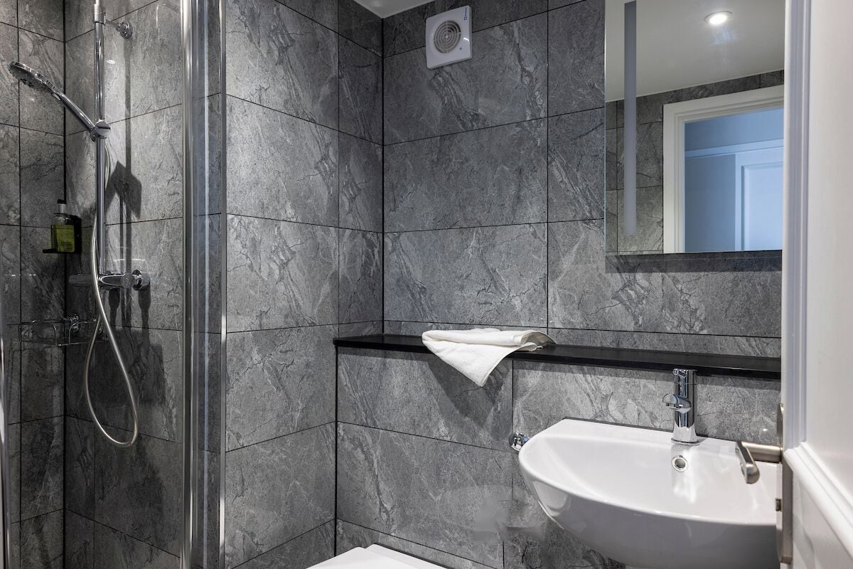 A modern bathroom with a glass-enclosed shower, a white sink, and a marble-tiled wall.
