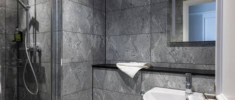 A modern bathroom with a glass-enclosed shower, a white sink, and a marble-tiled wall.