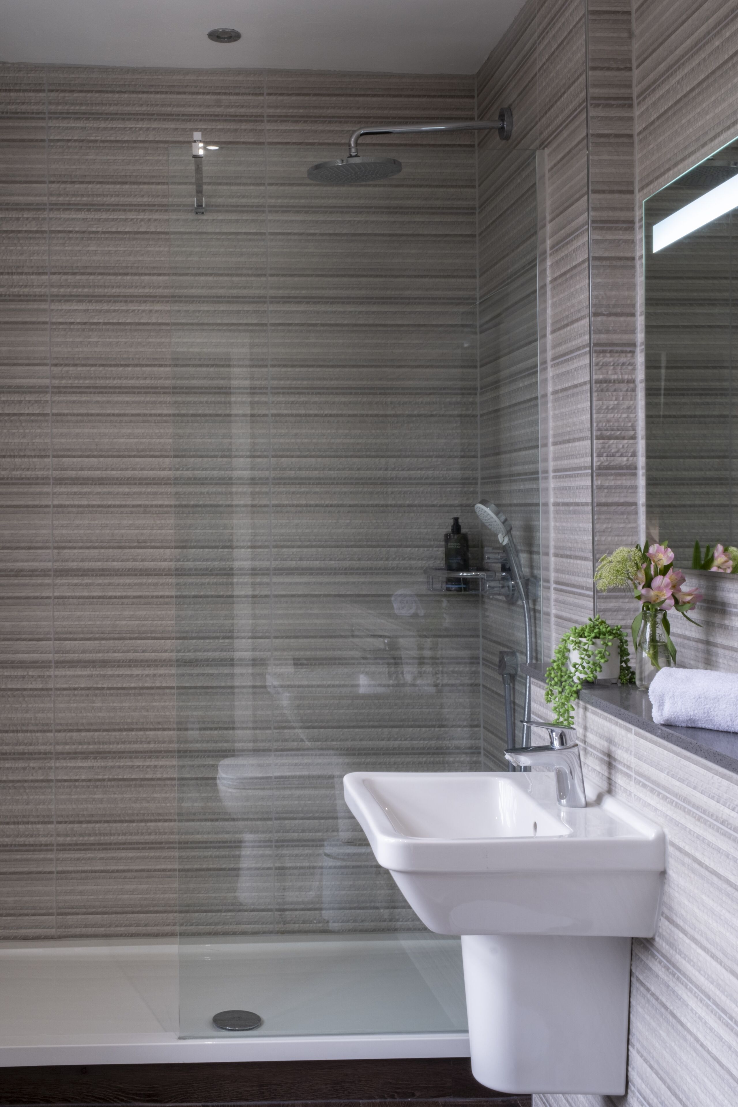 Un baño moderno con ducha envuelta en vidrio, un lavabo blanco y un espejo.