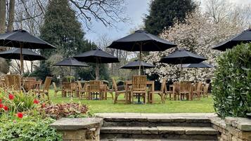 Een tuinpatio met stenen traptreden die leiden naar houten stoelen en tafels onder zwarte parasols.