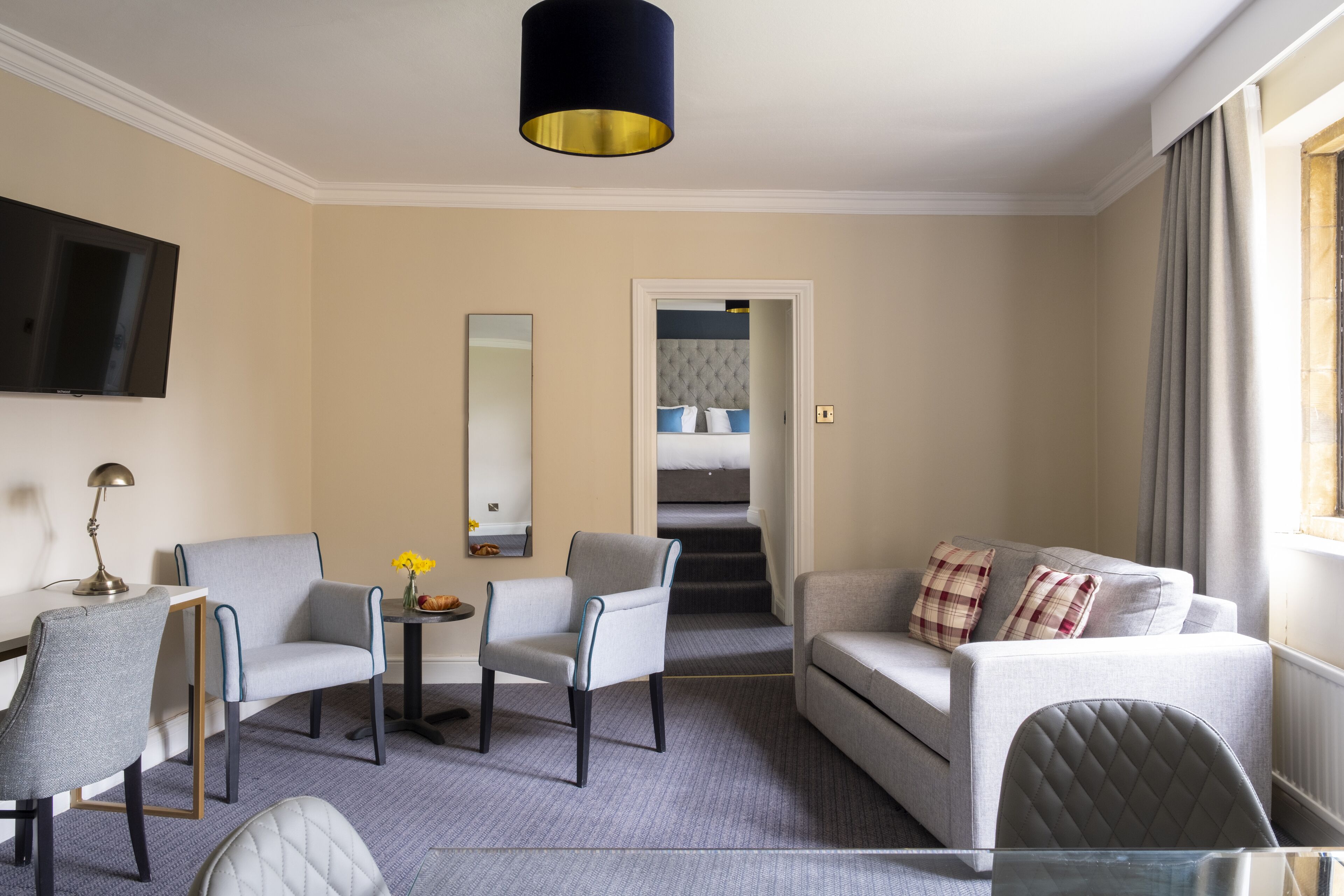 Habitación de hotel con sofá, dos sillones, una mesita con flores, televisión y espejo.