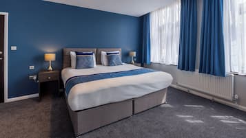 A hotel room with a large bed, two bedside tables, a lamp, and a window with curtains.