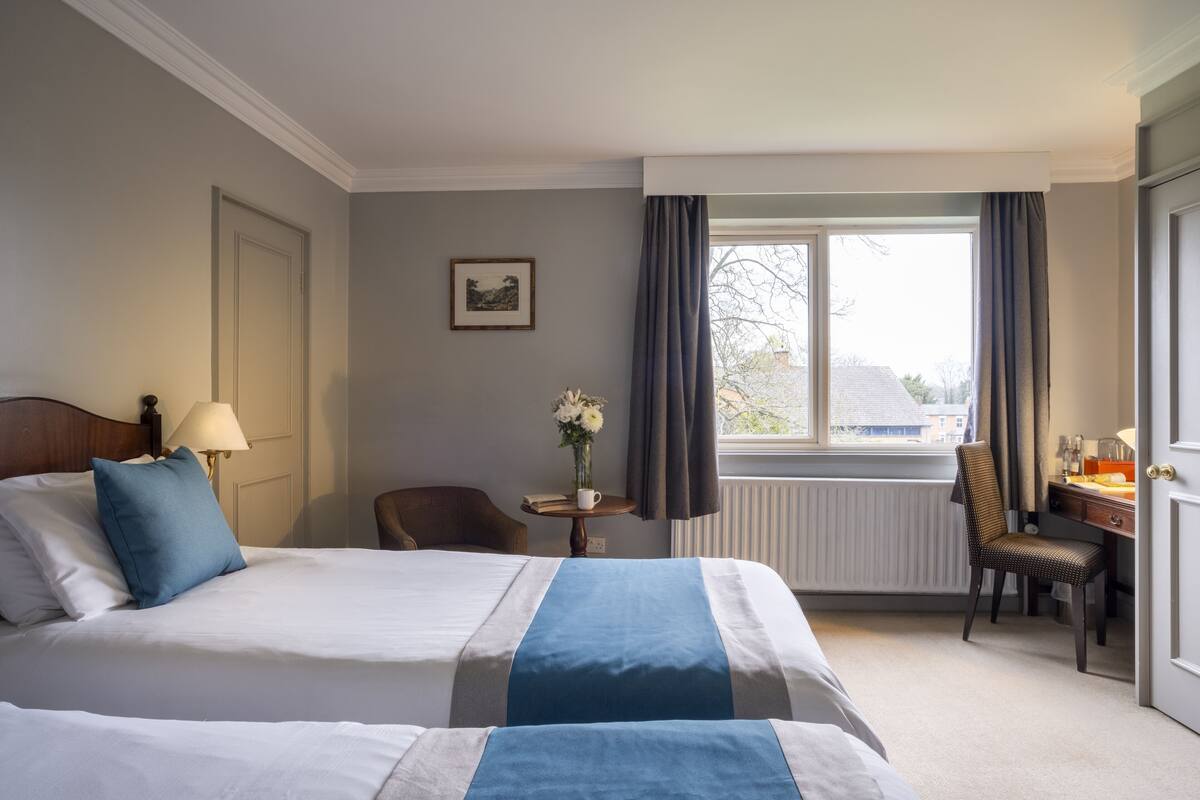 Une chambre d’hôtel avec un grand lit, un bureau, une chaise, une fenêtre avec des rideaux et un radiateur.