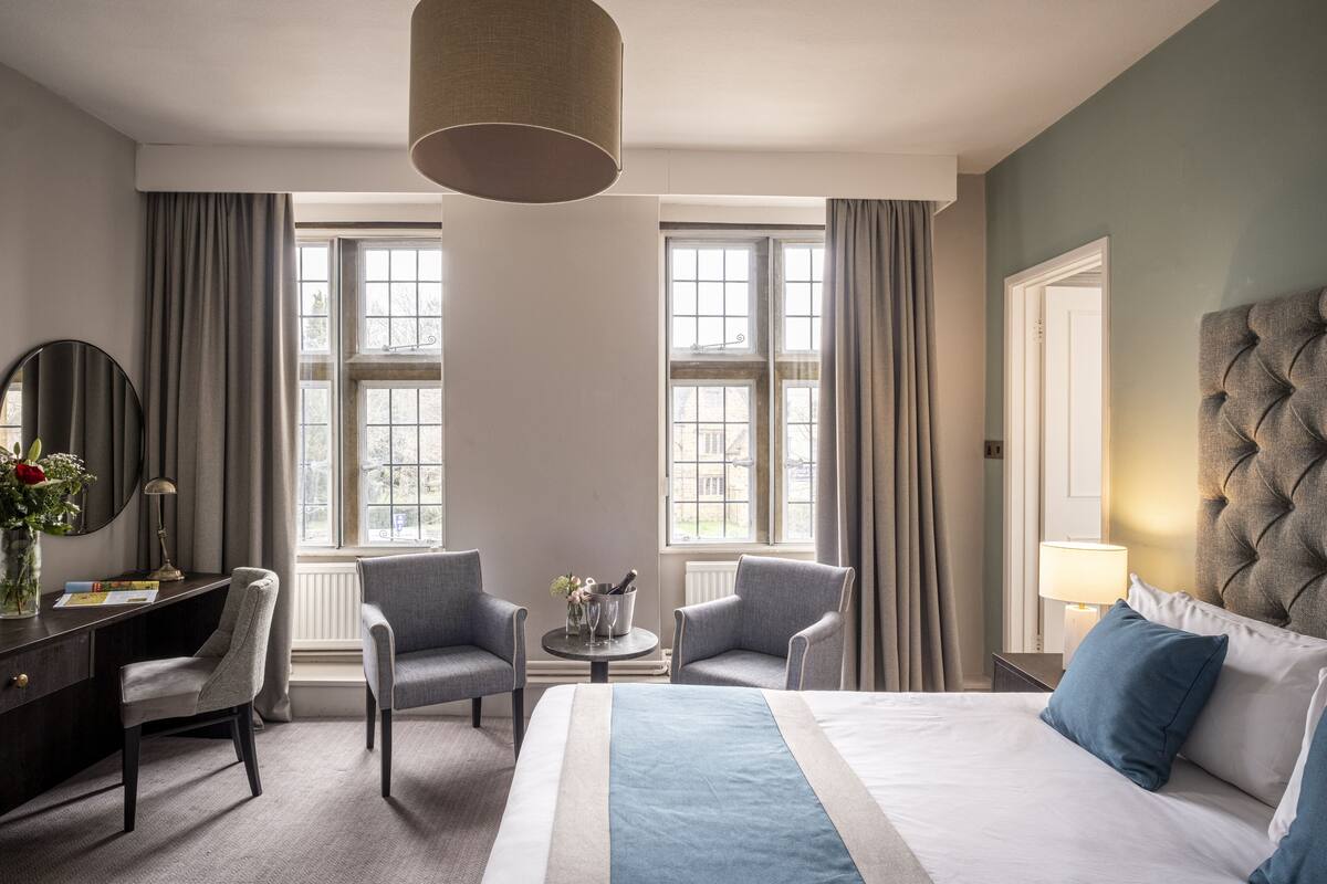 Une chambre d’hôtel avec un grand lit, deux fauteuils, un bureau et une petite table avec une lampe.