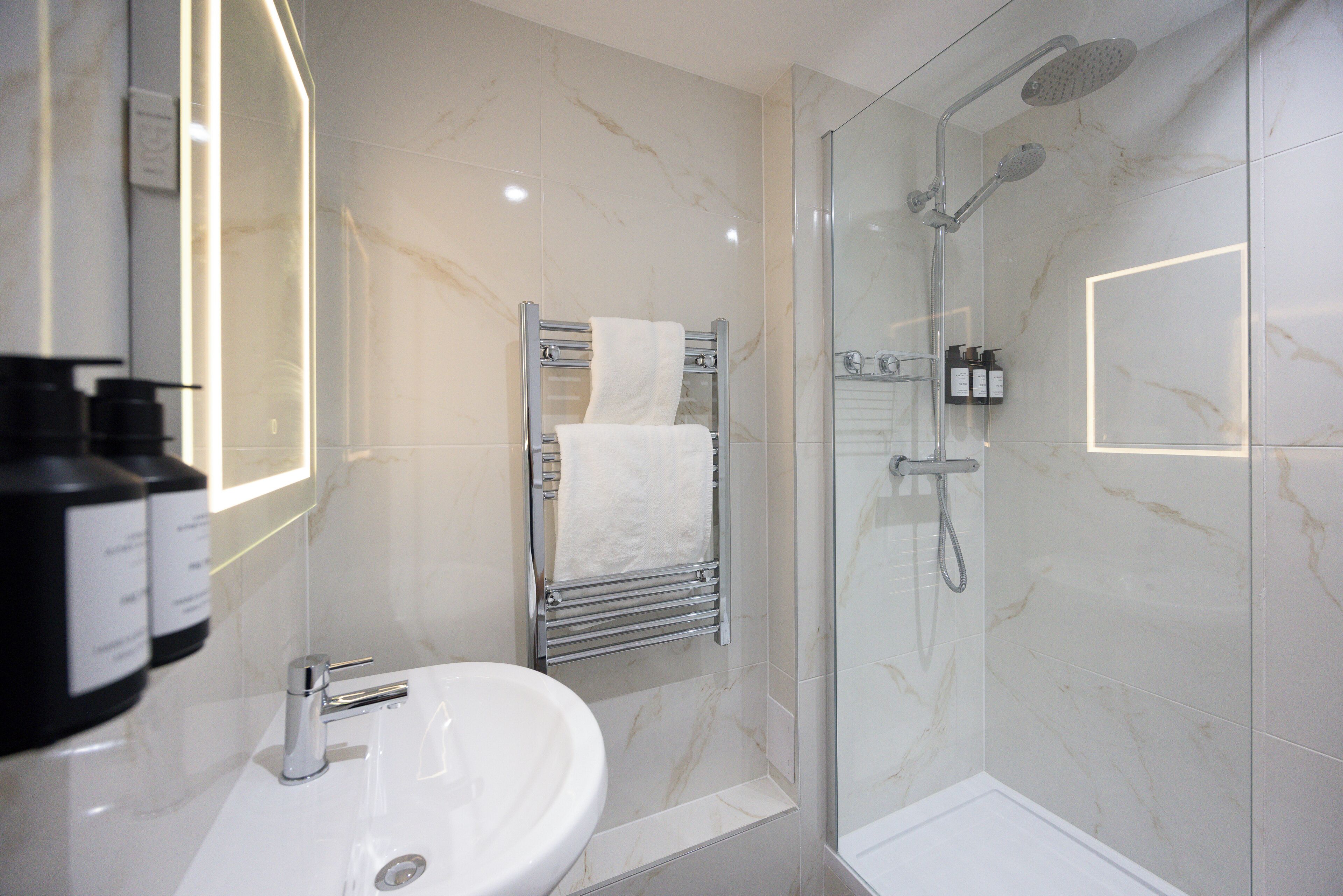 A modern bathroom with a white sink, a glass-enclosed shower, and a towel rack with a white towel.