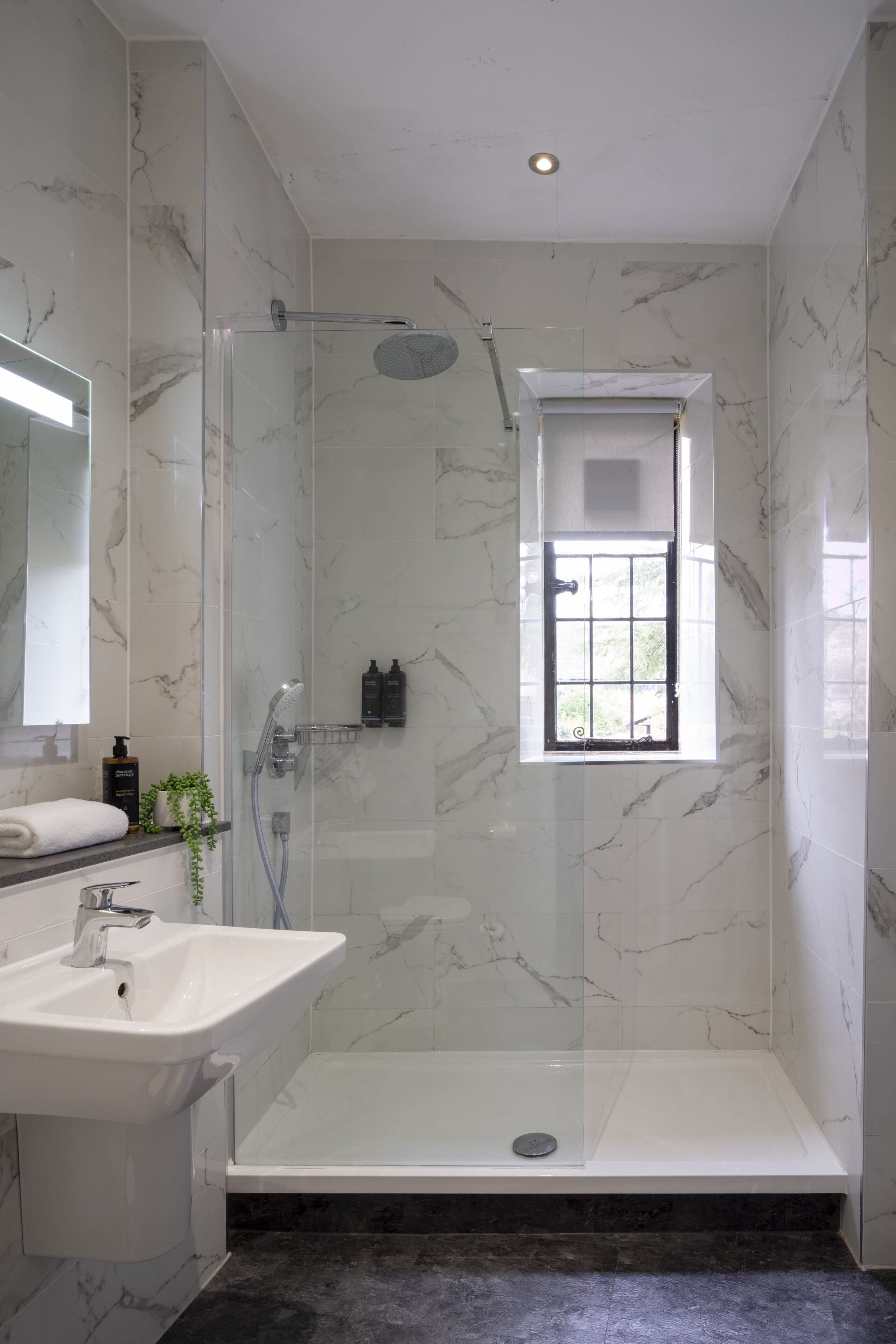 Une salle de bain moderne avec une douche en verre, un lavabo blanc et un mur recouvert de carreaux de marbre.