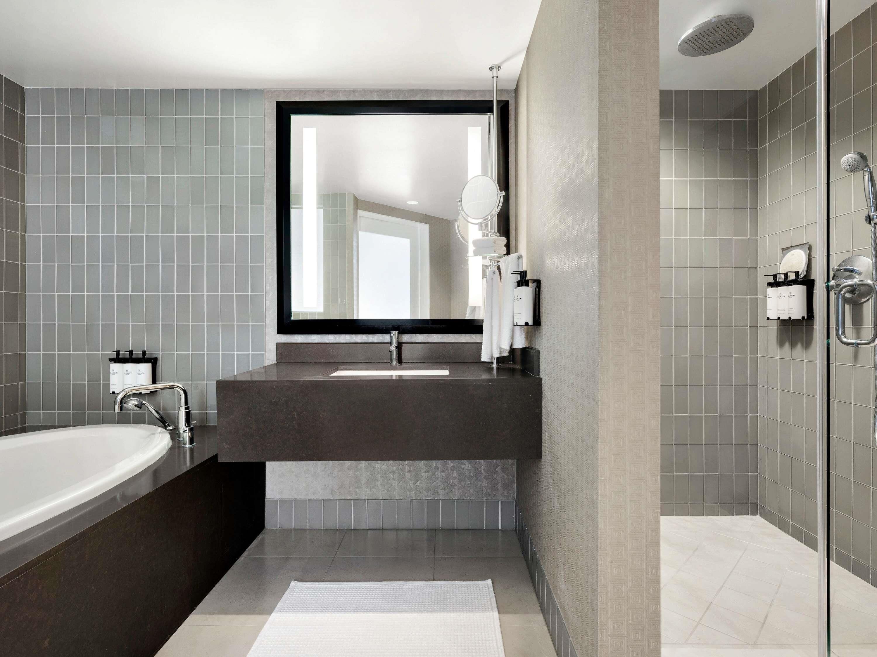 A modern bathroom with a large mirror, a bathtub, a shower, and a vanity with a sink.