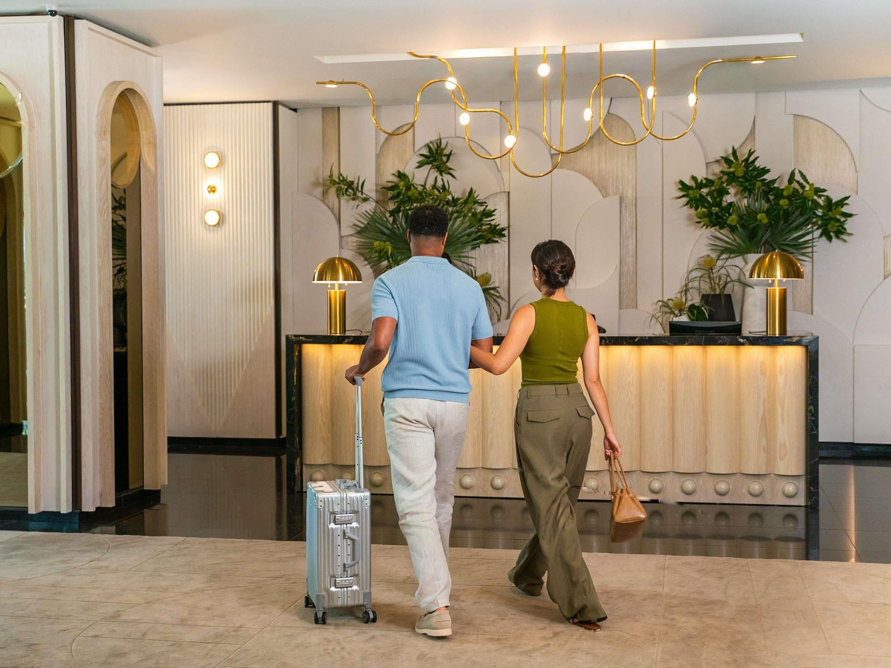 Uma receção com design moderno, um homem com mala e uma mulher a carregar uma bolsa.