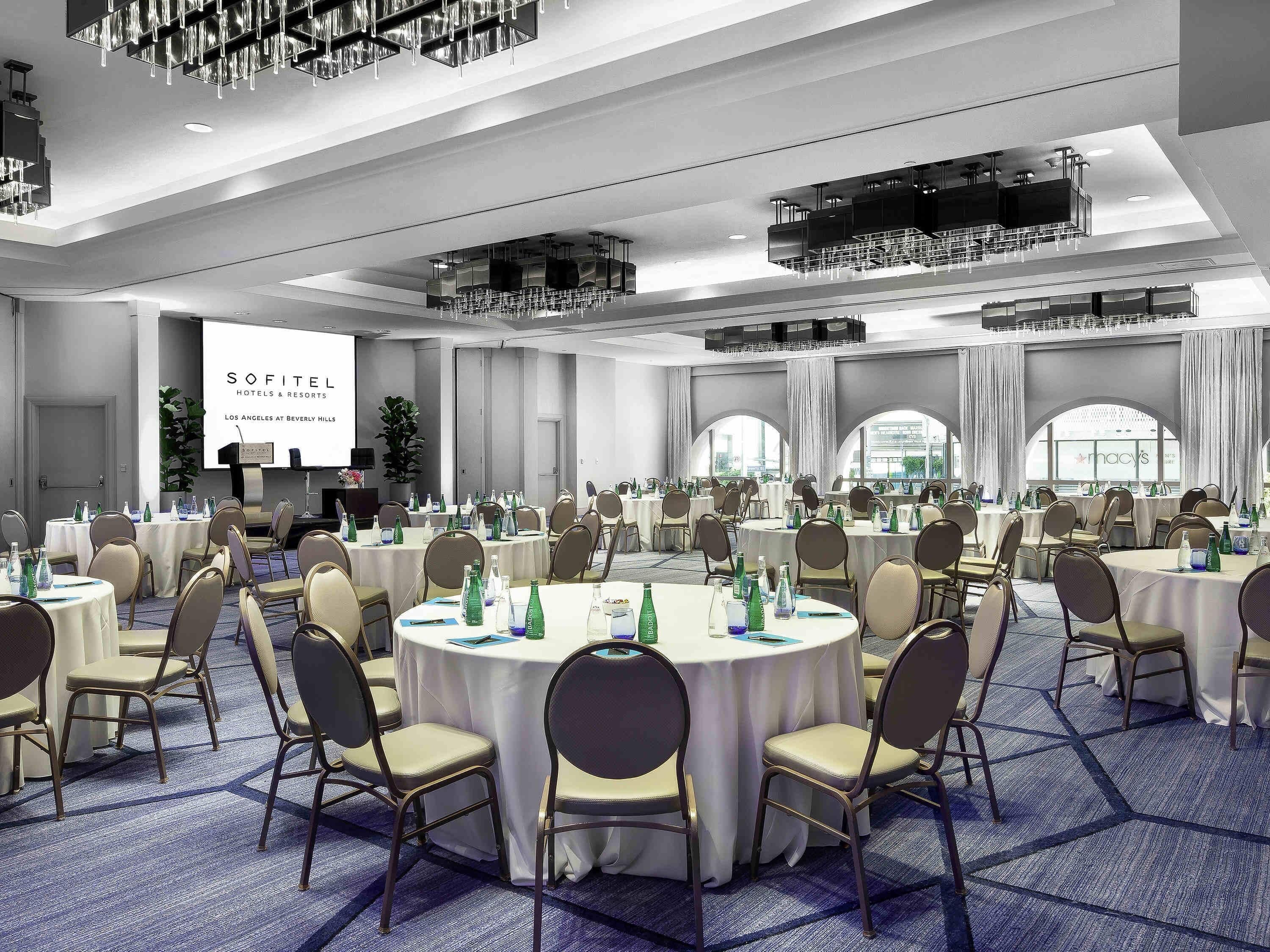Een congreszaal met ronde tafels, stoelen en een presentatiescherm.