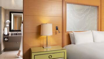 Hotelkamer met een bed, nachtkastje met een lamp, spiegel, badkamer met wastafel en handdoekhouder, en een houten wandpaneel.