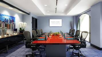 A conference room with a long table, chairs, a TV screen, and a cityscape painting.