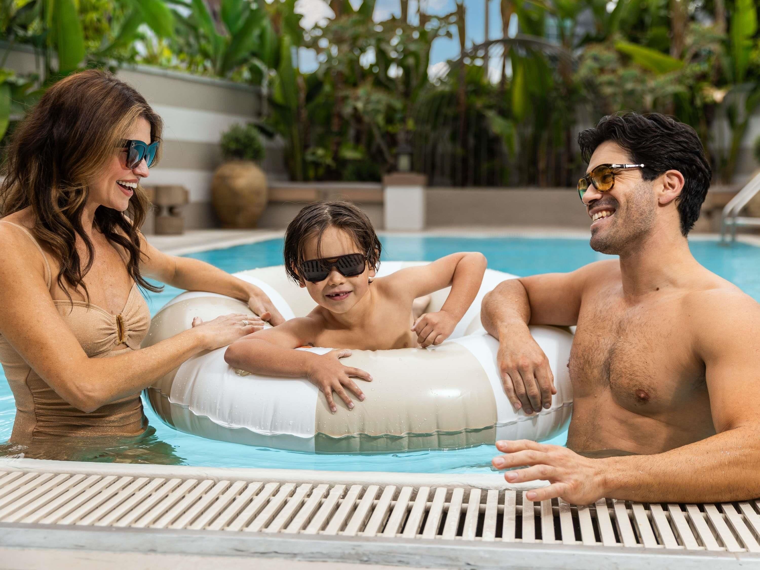 A family in a pool with a floating ring, surrounded by greenery.