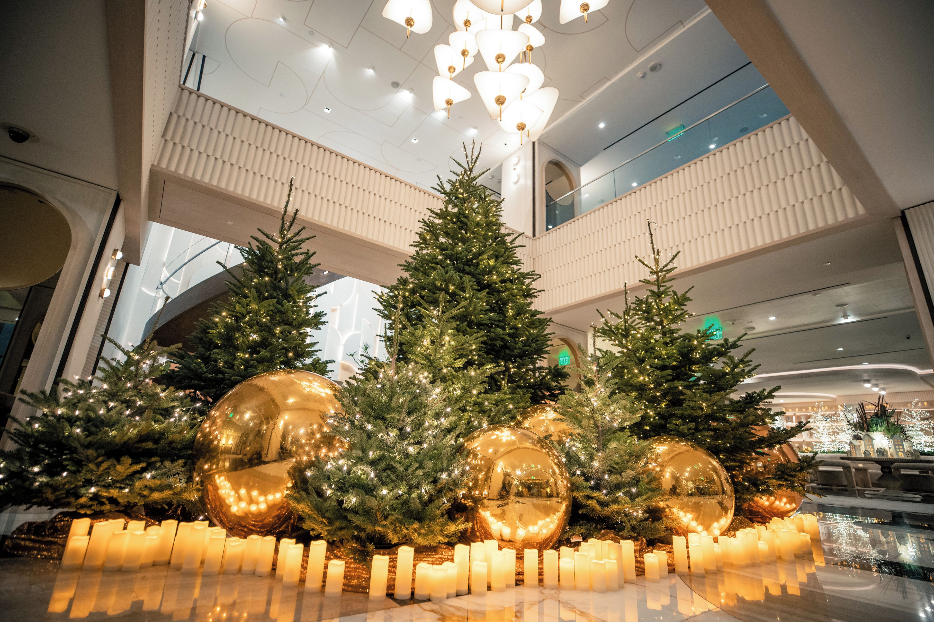 A spacious atrium with multiple Christmas trees and large golden ornaments.