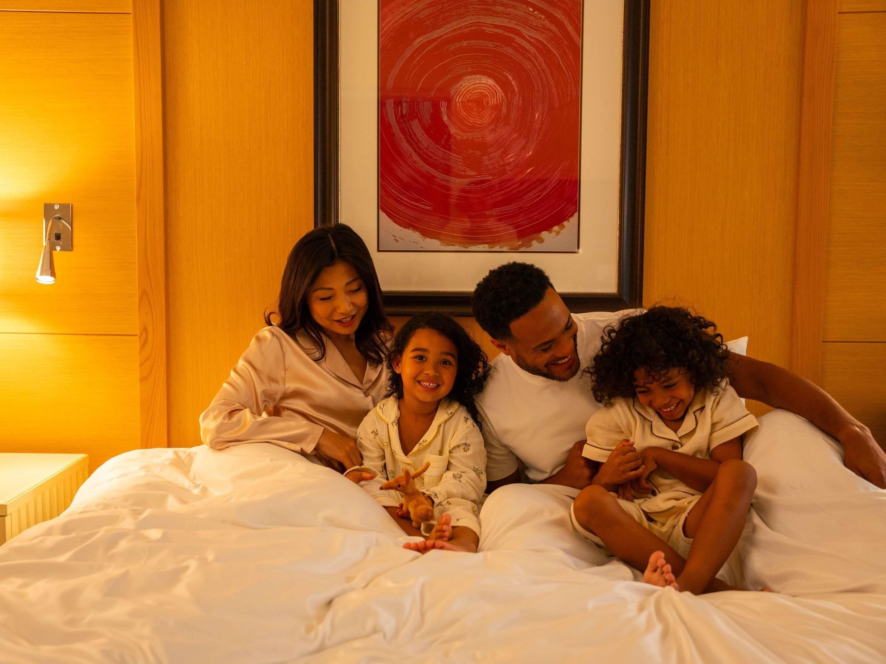 Una famiglia di quattro persone in una camera da letto con un grande letto, un comodino e un quadro appeso al muro.