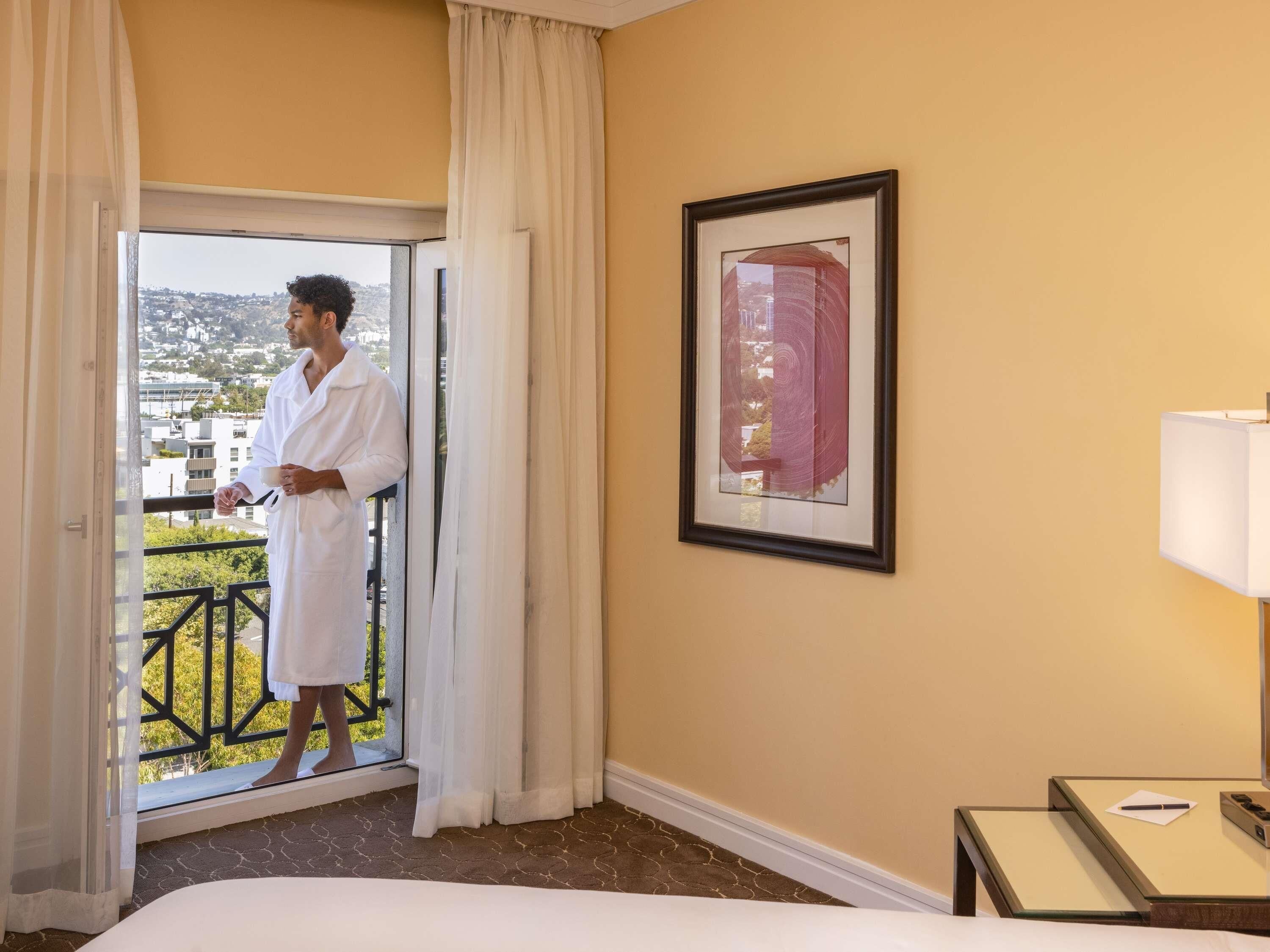 A hotel room with a balcony, a bed, a framed picture, and a bedside table with a lamp.