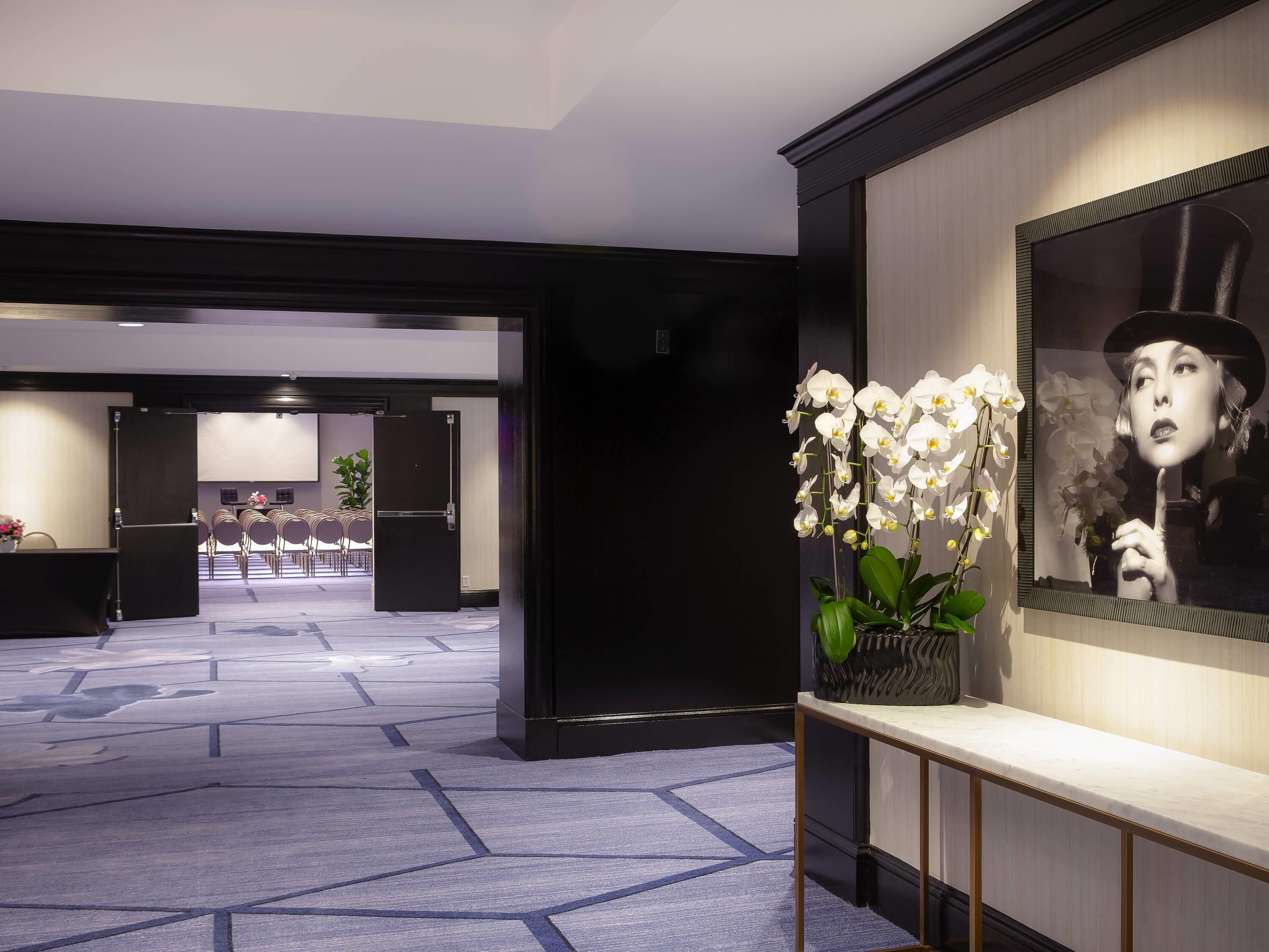 A hotel lobby with a reception desk, seating area, and a large mirror with an orchid arrangement.