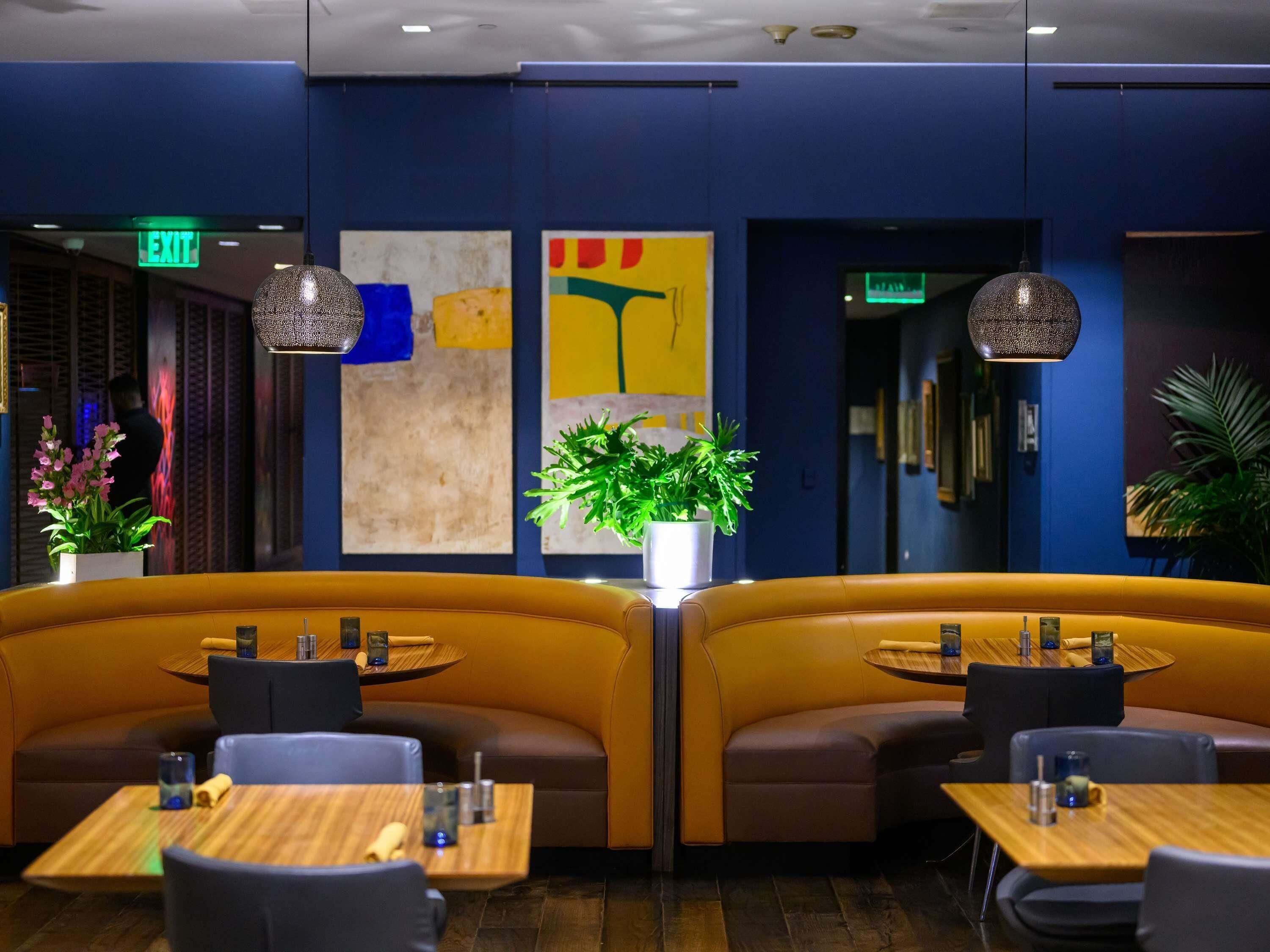 A restaurant with booths and tables, a green exit sign, and abstract wall art.