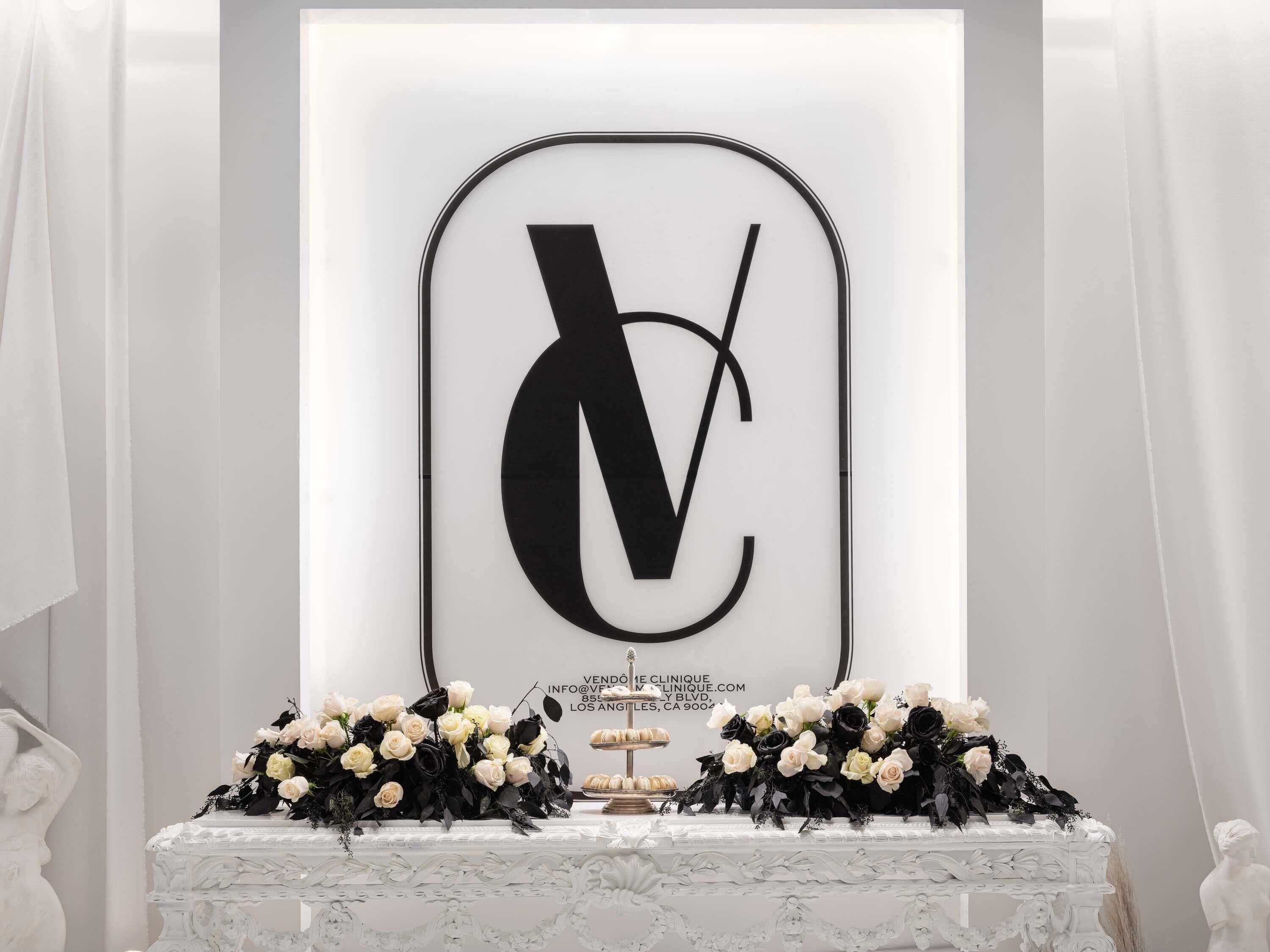 A white table with a large black and white letter 'V' framed in a black border, surrounded by white and black flowers.