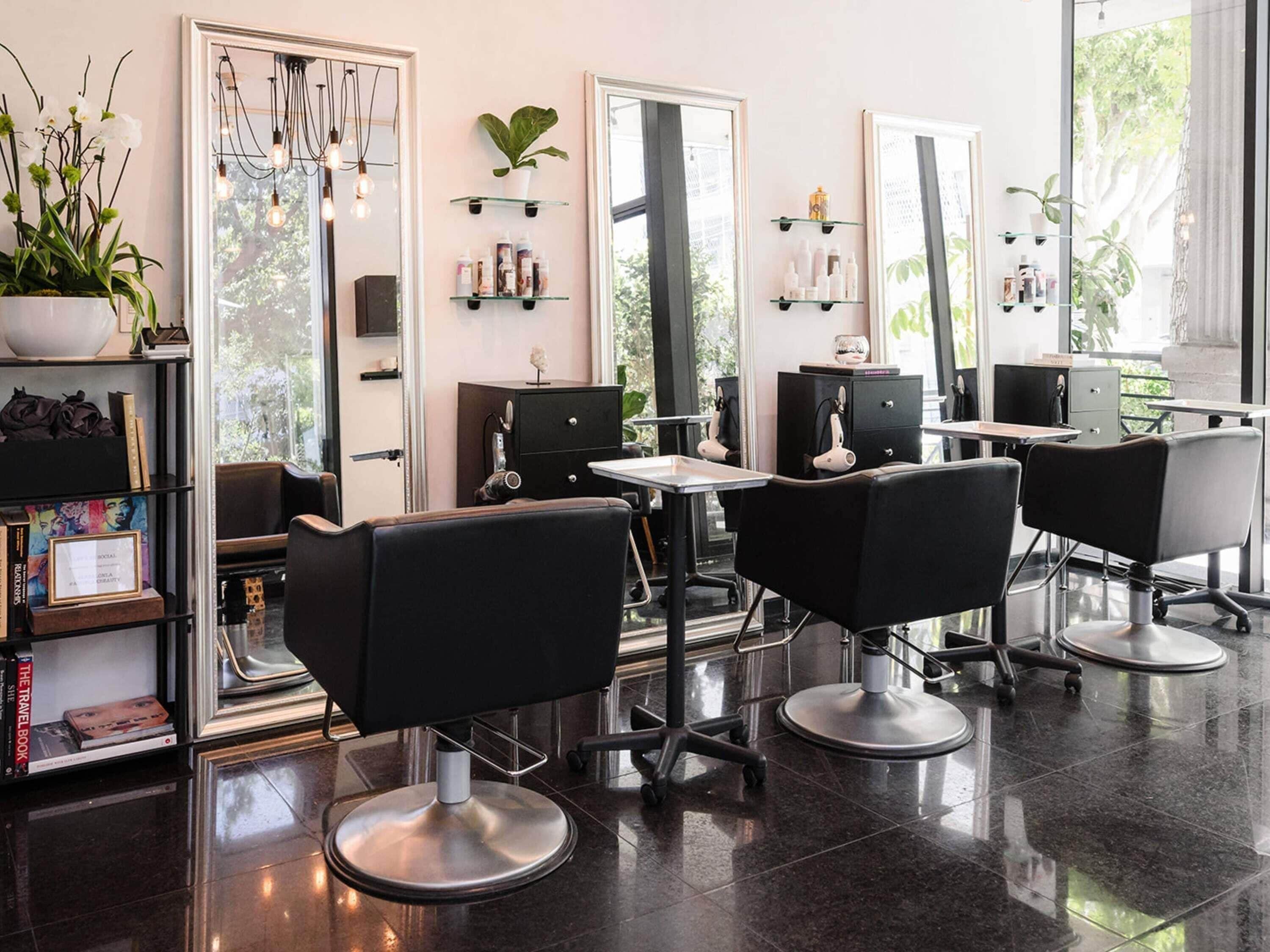 A salon with black chairs, a mirror, shelves with products, and a potted plant.