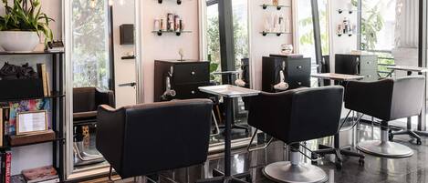 A salon with black chairs, a mirror, shelves with products, and a potted plant.