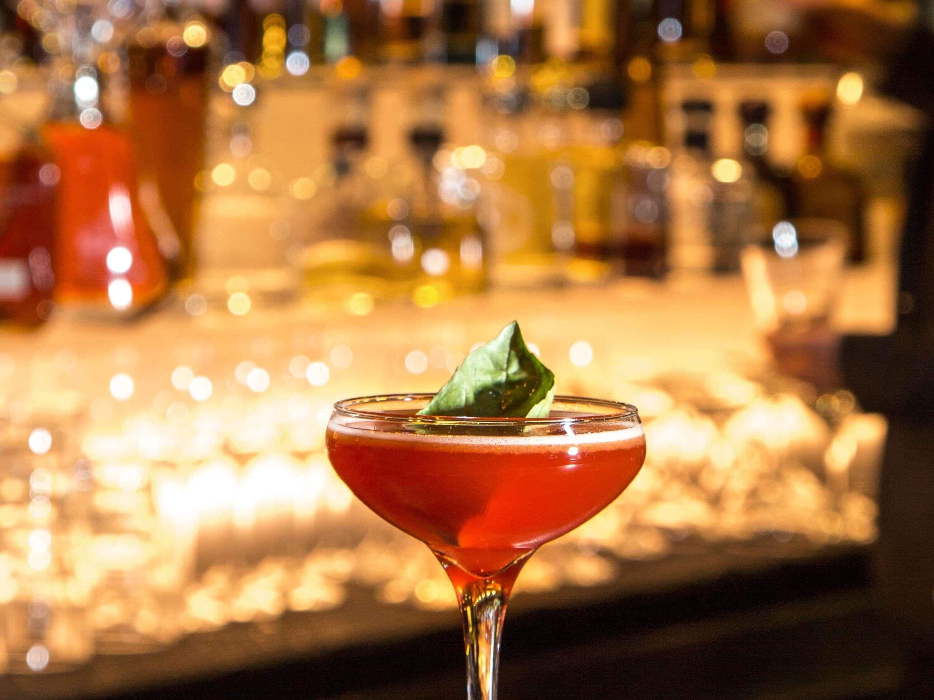 Un cocktail servi dans un verre à martini, agrémenté d’une garniture, sur fond flou d’étagères de bar.