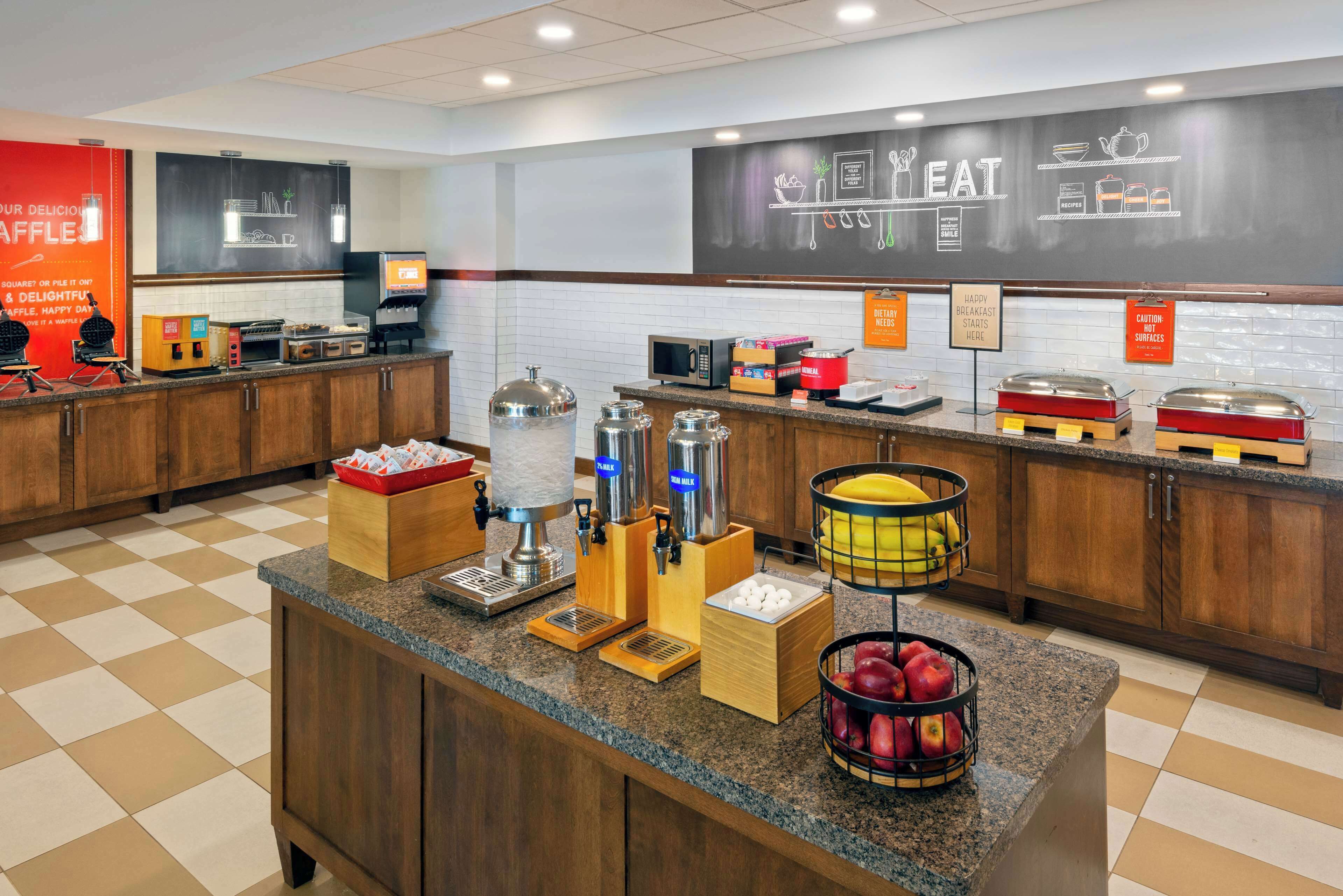A buffet counter with various food items and appliances, including a coffee machine and a fruit basket.