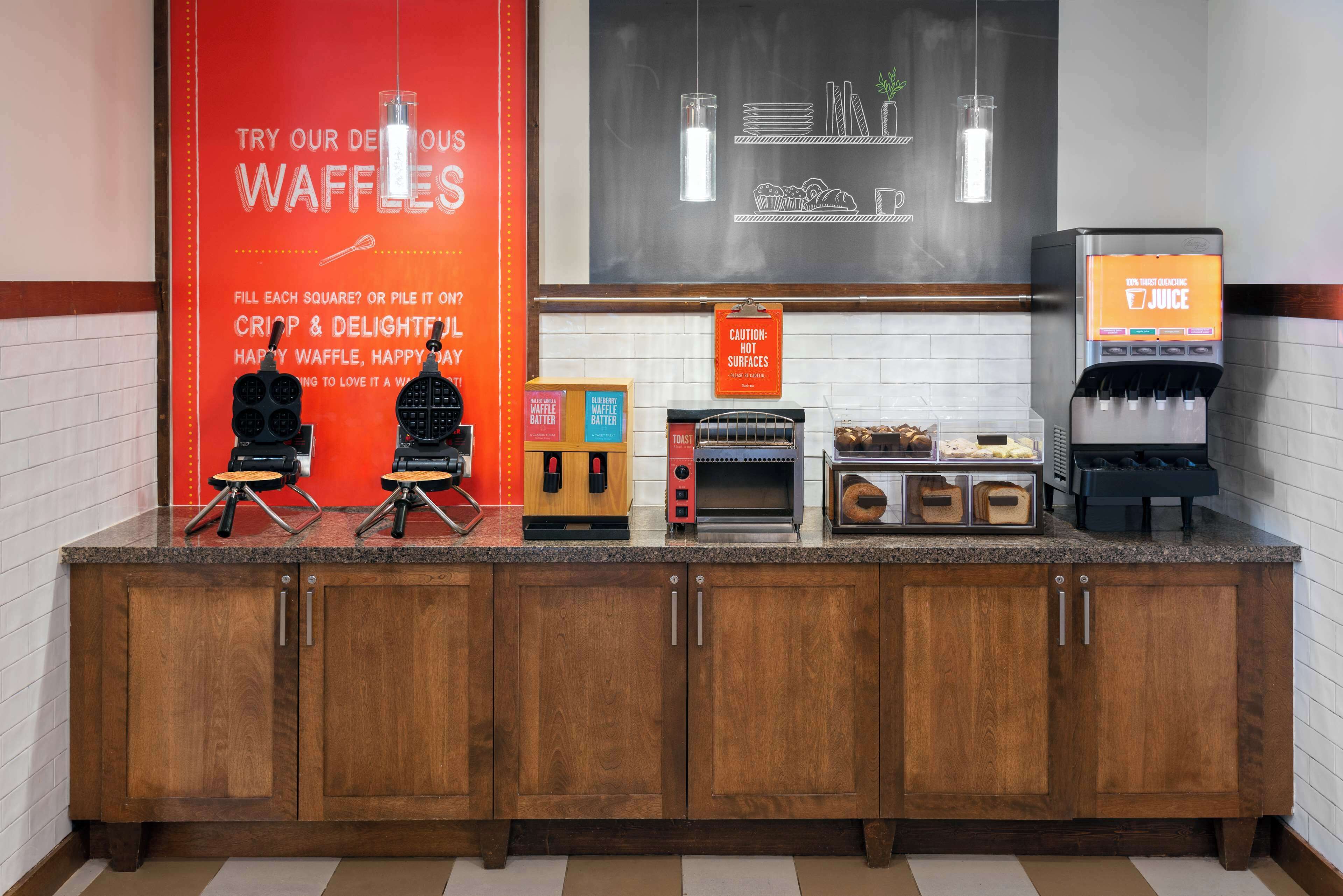 A kitchen counter with waffle makers, a toaster, and a juice dispenser.