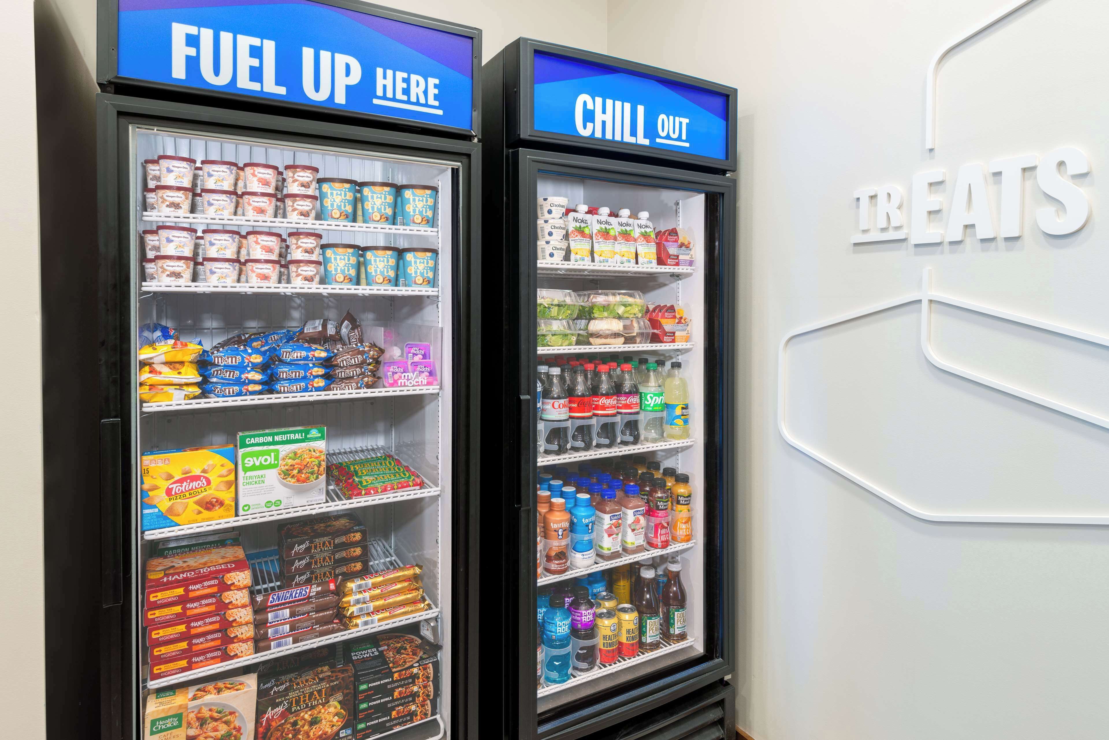 Zwei gekühlte Getränkespender, beschriftet mit „FUEL UP HERE“ und „CHILL OUT“, mit verschiedenen Getränken und Snacks.