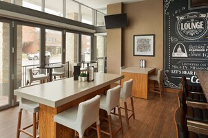 A modern lounge with a long counter, bar stools, and a large window offering a view of the street.