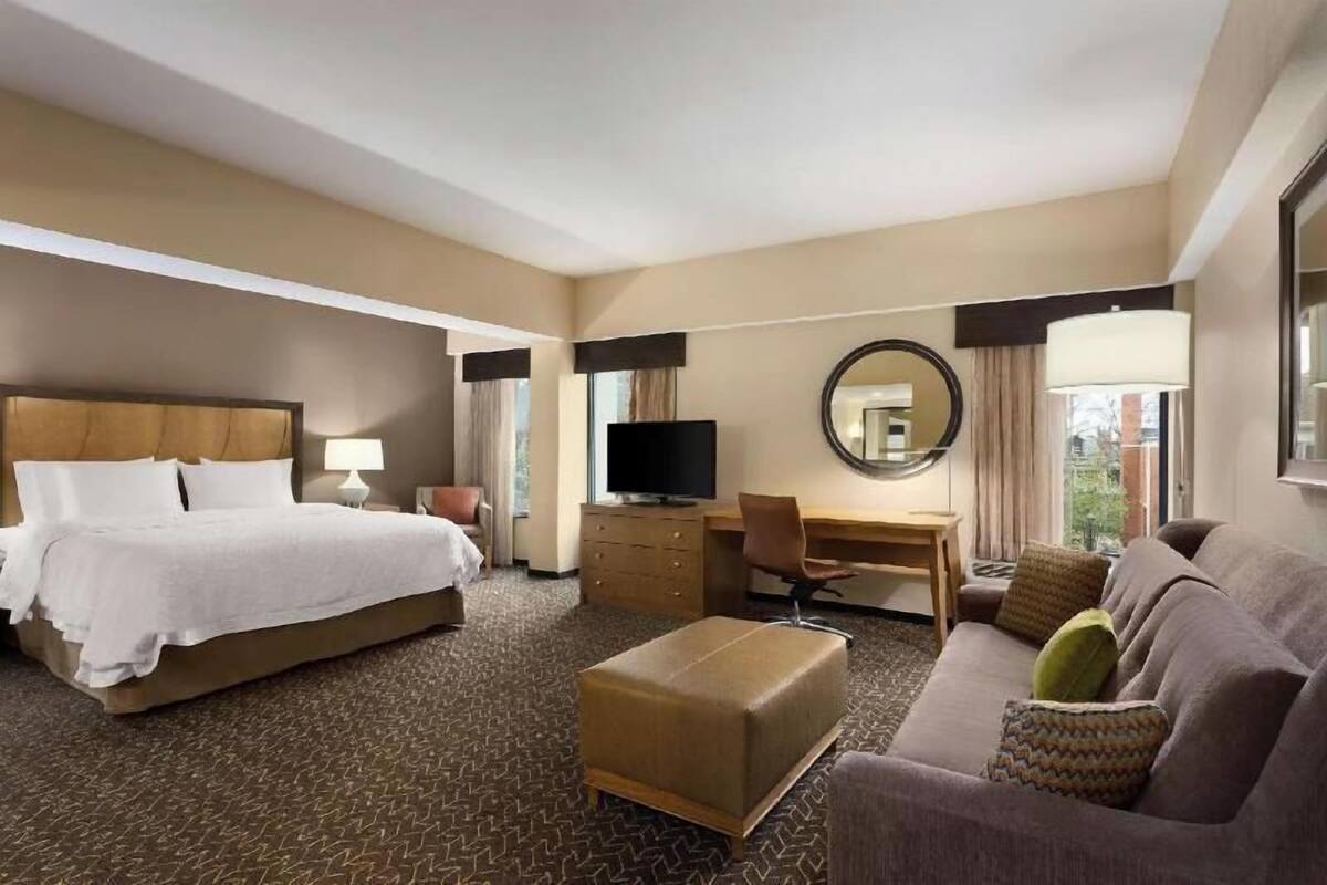 A hotel room with a bed, a desk, a television, a sofa, and a mirror.
