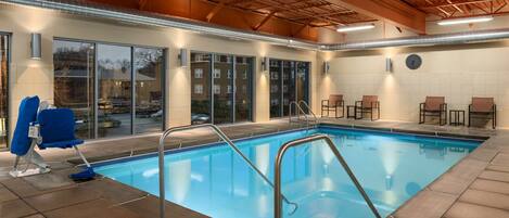 An indoor swimming pool with clear water, surrounded by lounge chairs and a tiled floor.