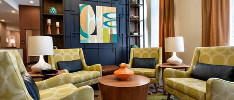 A modern lounge area with yellow patterned armchairs, a central wooden coffee table, and a large abstract painting on the wall.