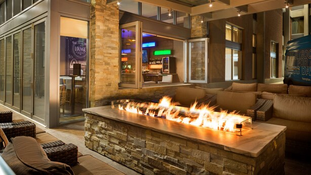 Ein moderner Lounge-Bereich mit Kamin aus Naturstein, bequemen Sitzgelegenheiten und einer Bar im Hintergrund.
