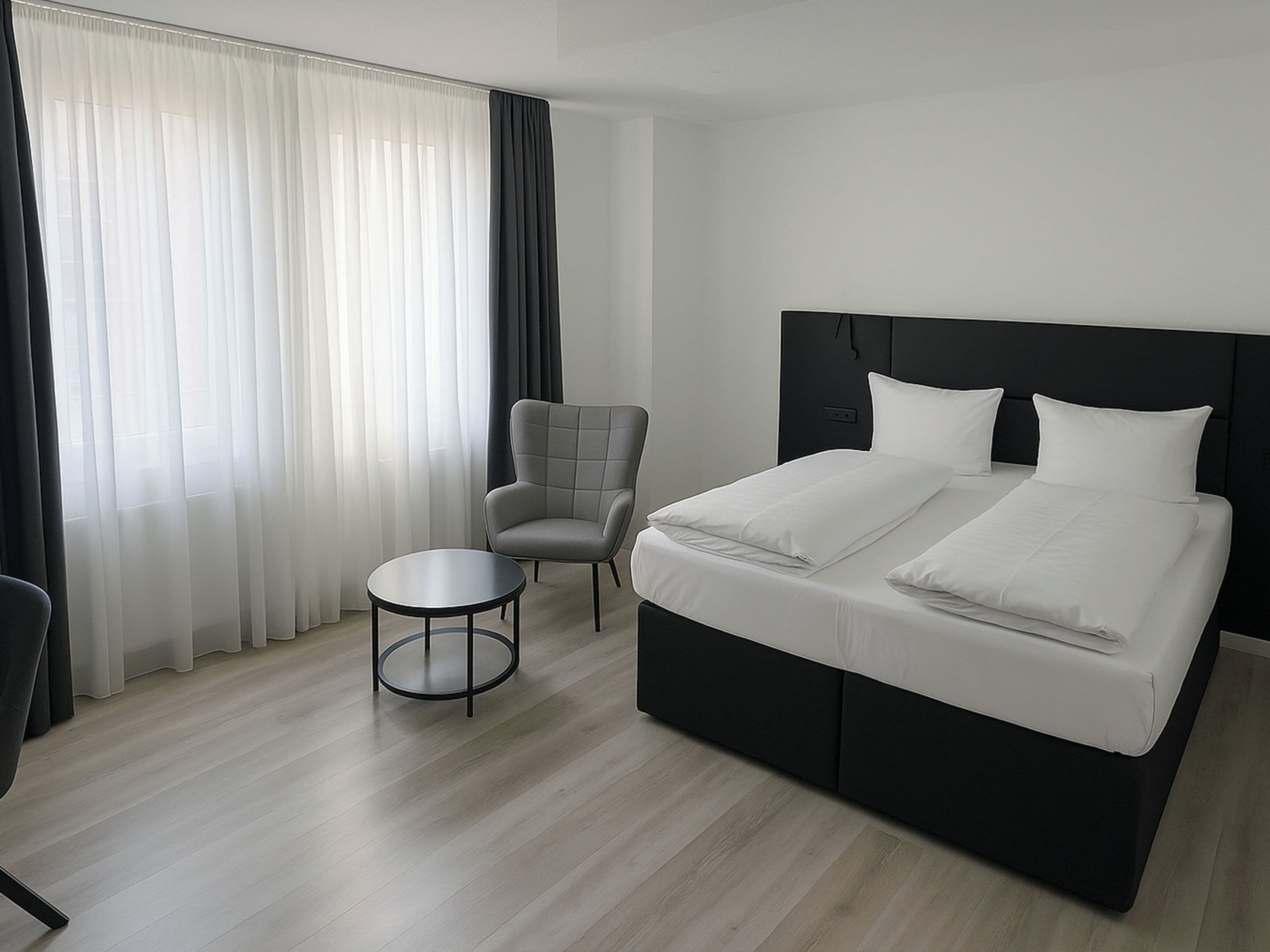A modern hotel room with a large bed, a small round table, and a chair.