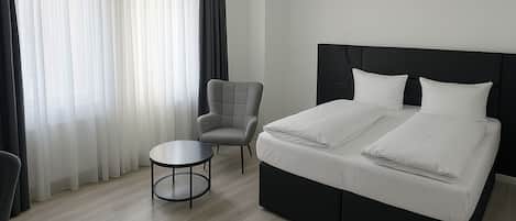 Ein modernes Hotelzimmer mit einem großen Bett, einem kleinen runden Tisch und einem Sessel.