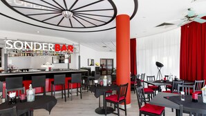 A modern bar area with a 'Sonder Bar' sign, red and black chairs, and a unique ceiling design. - Dormero Hotel Dessau-Rosslau (Dessau-Rosslau)