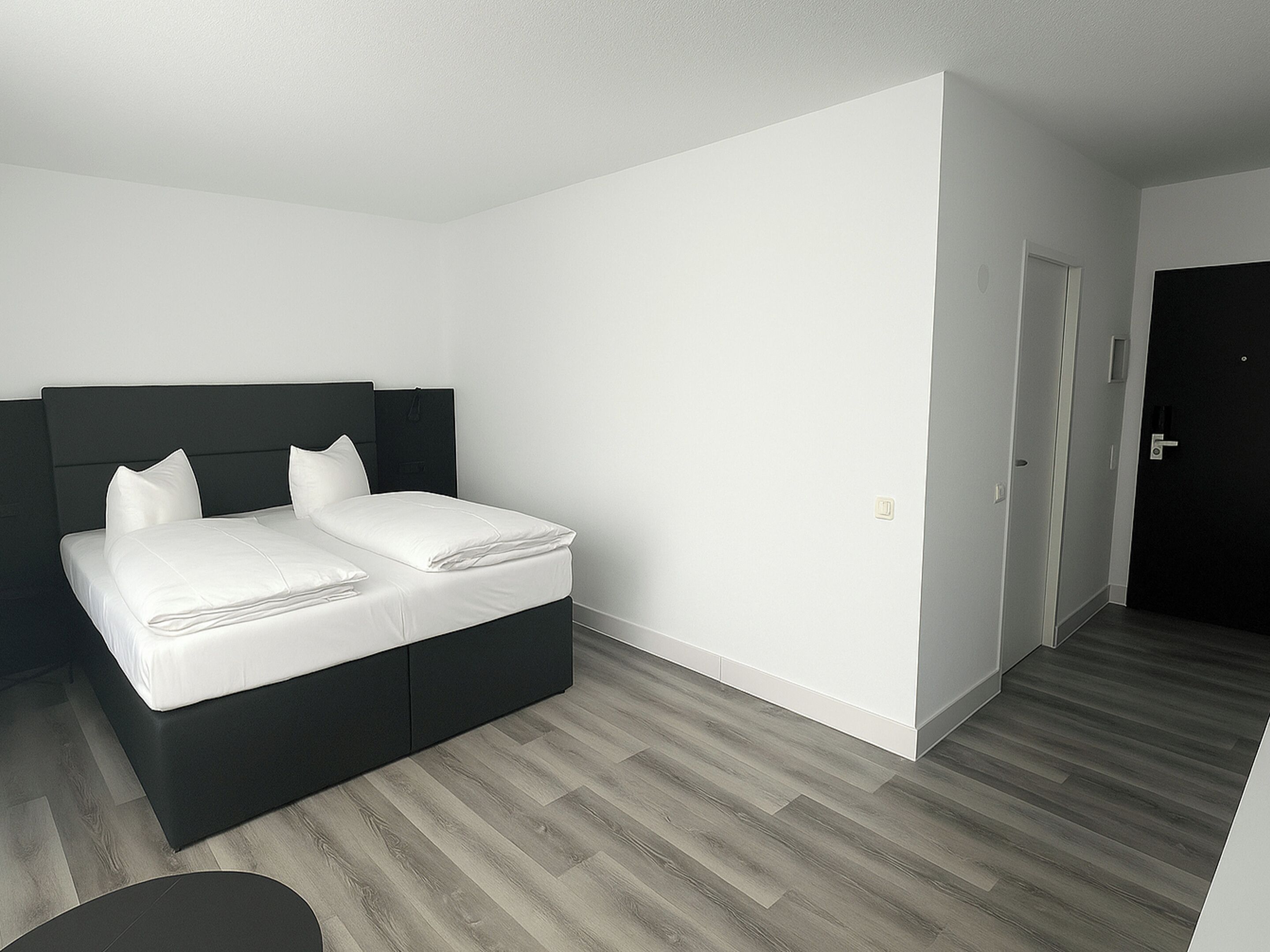 A modern bedroom with a bed, a dark headboard, and a wooden floor.