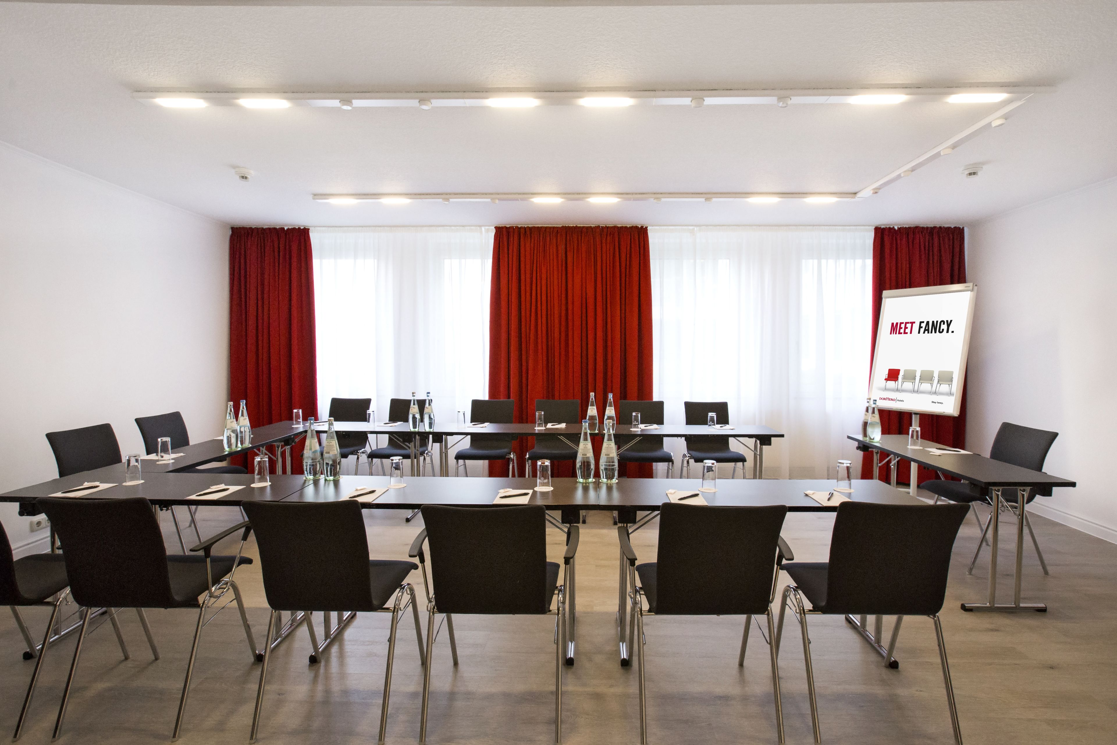 A conference room with a long table, black chairs, and a presentation screen.