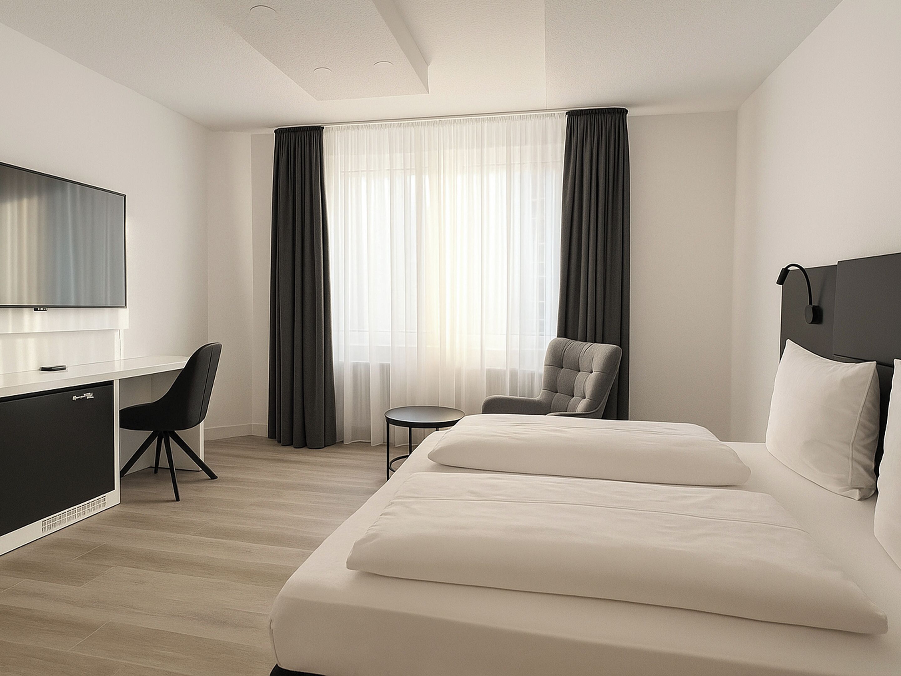A modern hotel room with a bed, a desk, a chair, and a TV.