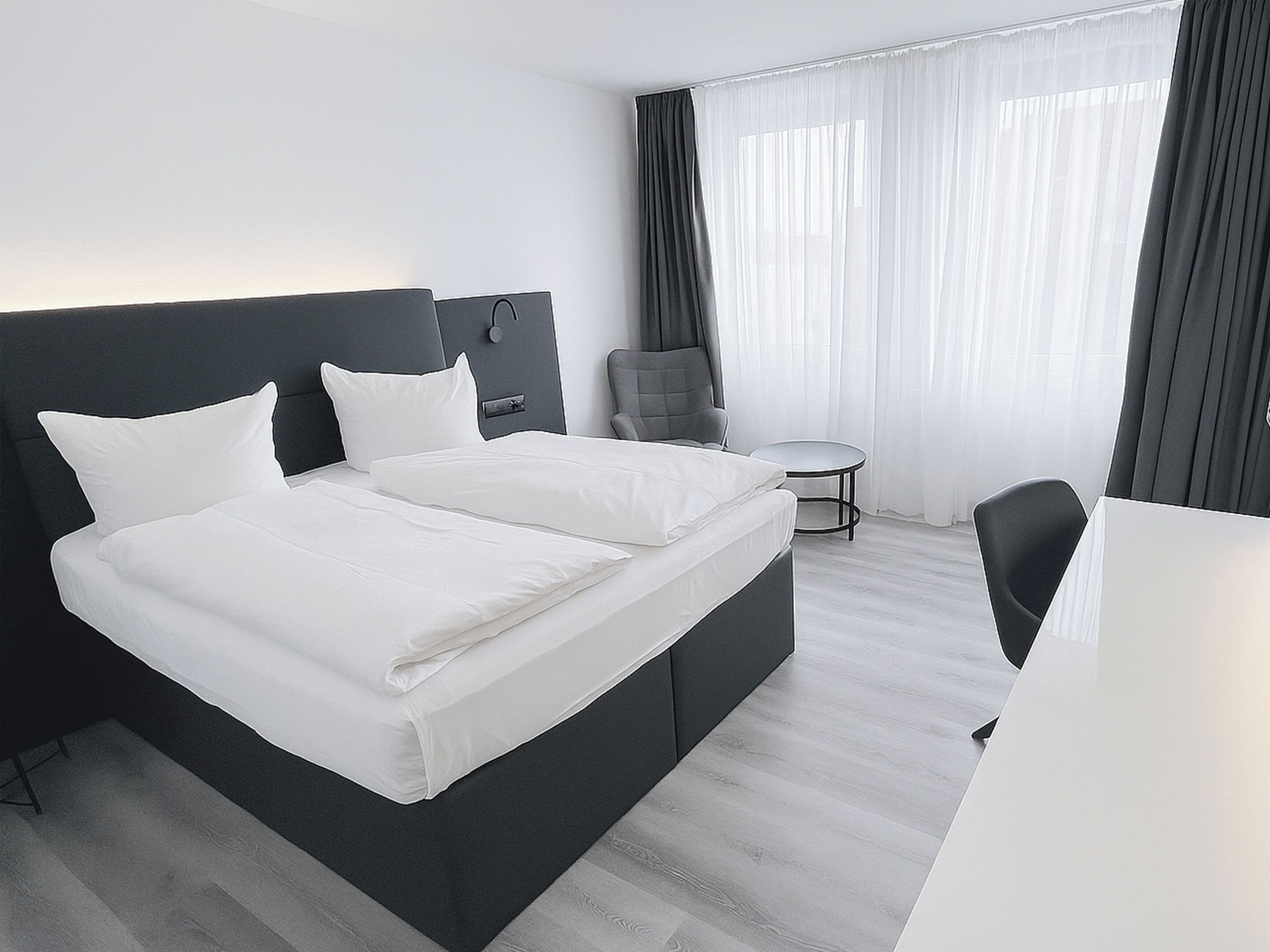 A modern hotel room with a large bed, a desk, and a chair.