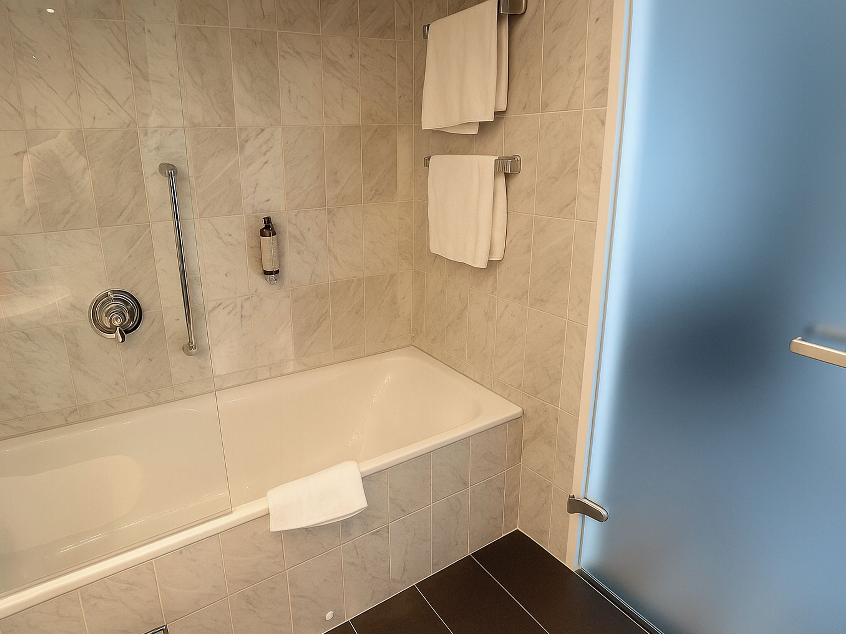 Ein modernes Badezimmer mit einer Badewanne, einer Dusche und einem WC. Handtücher hängen an der Wand und eine Shampooflasche steht auf dem Boden.