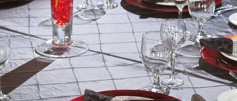 A dining table set with red and white plates, silverware, and clear wine glasses.