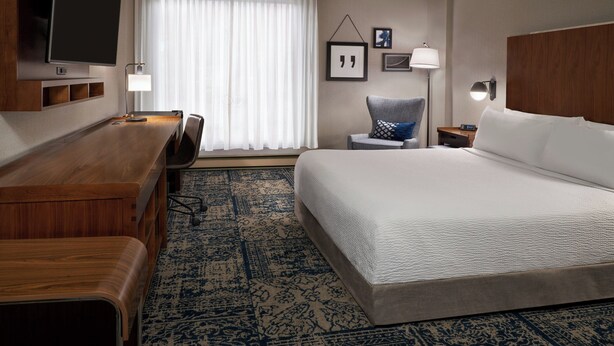 A hotel room with a large bed, a desk with a chair, a television mounted on the wall, and a window with curtains.