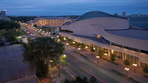 A modern building with a curved roof and multiple levels, surrounded by a parking lot and a street with streetlights.