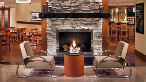 A lobby with a stone fireplace, two armchairs, a bar area, and a dining area with wooden tables and chairs.