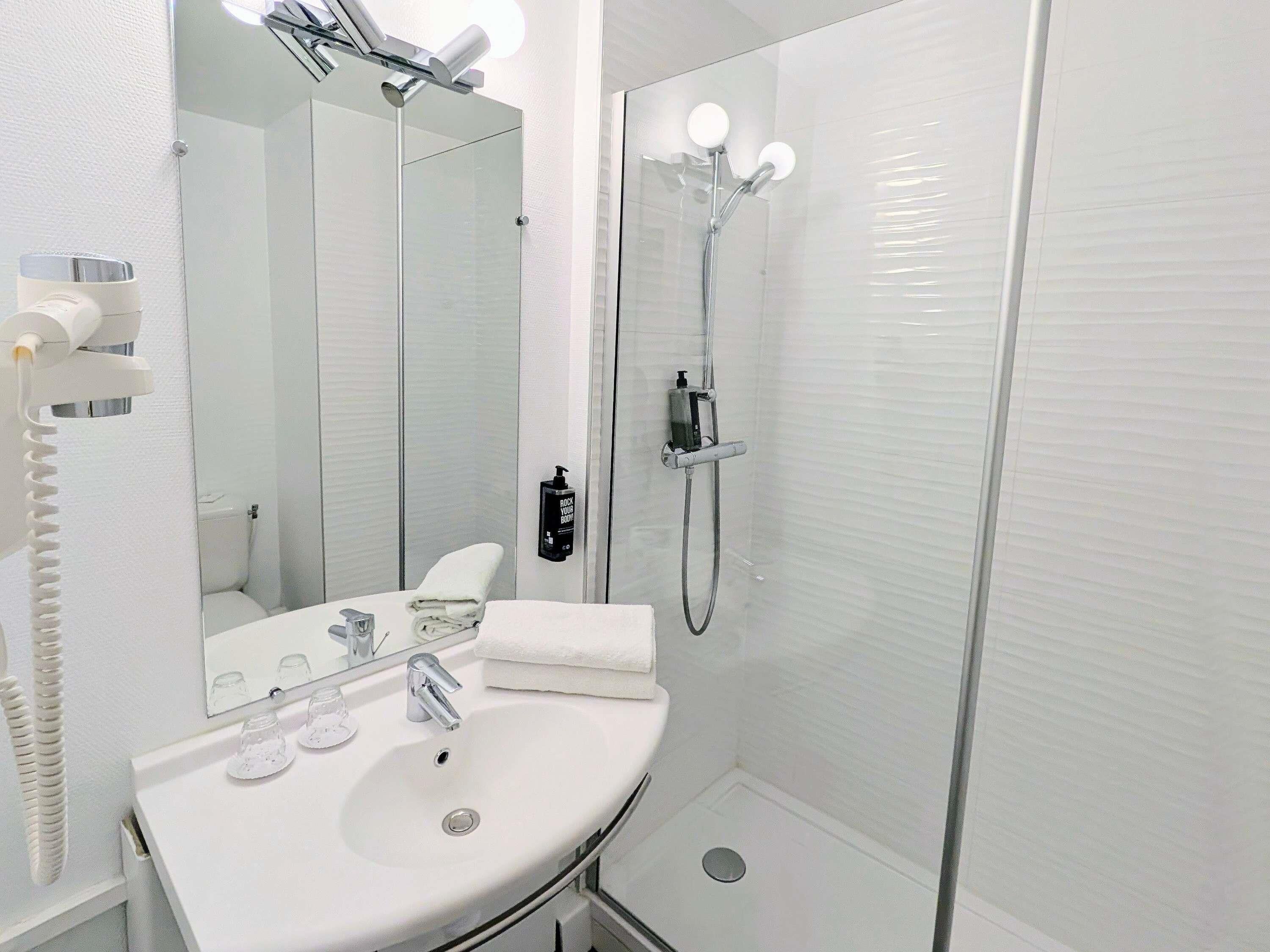 A modern bathroom with a white sink, mirror, and glass-enclosed shower.