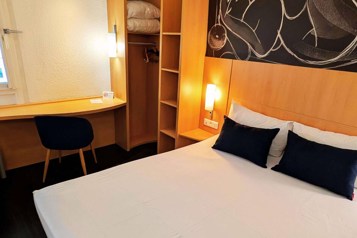 Ein Hotelzimmer mit einem Bett, einem Schreibtisch, einem Stuhl, einem Kleiderschrank und einer Wand mit dekorativer Gestaltung.