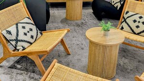 Sillas de mimbre con cojines estampados, una mesa redonda de madera y una pequeña planta en maceta.